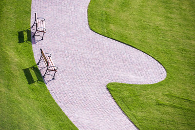 Cobbled park alleys and a wooden park bench. all surrounded by green grass on a sunny, bright day