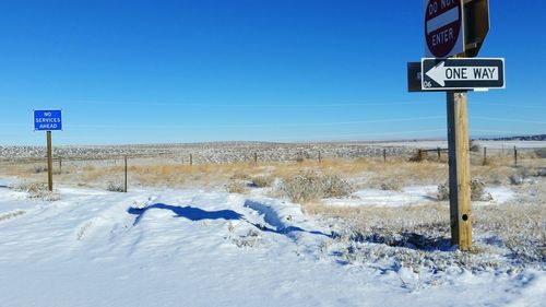 Road sign on snow covered field against clear blue sky