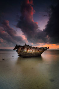 Broken boat against sky at beach during sunset