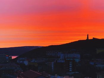 Silhouette buildings in city against orange sky