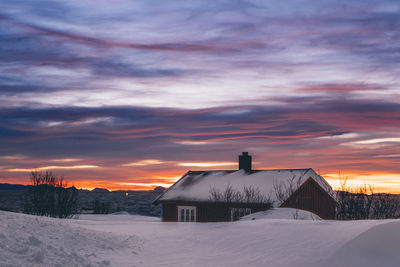 House on snow covered field against sky during sunset