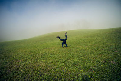 Full length of man doing handstand on grassy field against sky