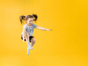Full length of young woman exercising against yellow background