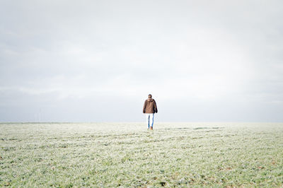 Rear view of man walking on grassy field against sky