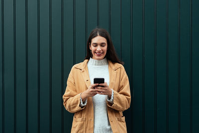 Smiling young woman using mobile phone while standing outdoors