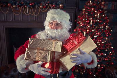 Man wearing santa claus costume holding christmas presents at home