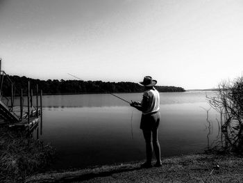 Rear view of man fishing in lake against clear sky