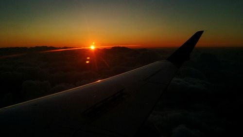 Airplane wing over landscape against sunset sky