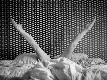 Low section of young woman with legs apart on bed against wall