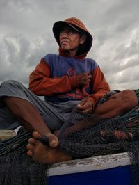 Low angle view of man sitting on fishing boat against sky