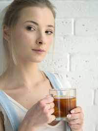Young woman holding drink while standing against wall