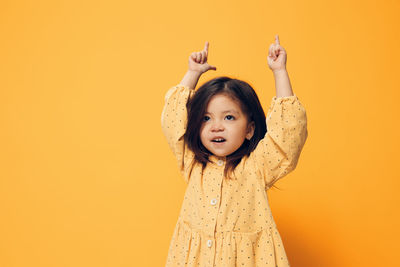 Cute girl with arms raised against orange background