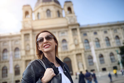 Smiling woman in sunglasses standing against kunsthistorisches museum