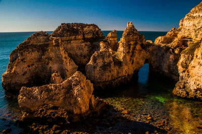 Rock formations in sea against clear blue sky