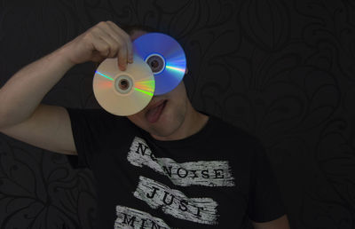 Man holding compact discs while standing against wall