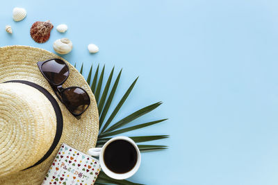 Hat with sea shells, palm leaf, passport, eyeglasses and cup of coffee on blue background