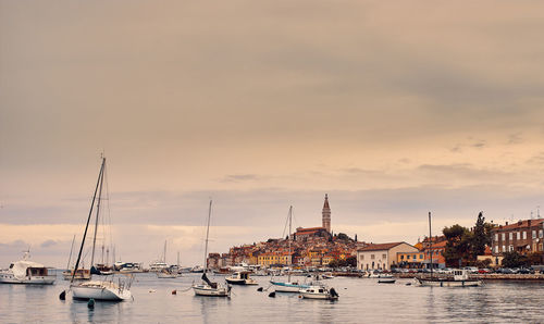 Sailboats moored at harbor against sky during sunset