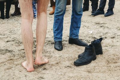 Low section of wet barefoot man standing with friends wearing shoes at beach