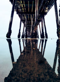 Reflection of pier on sea against clear sky