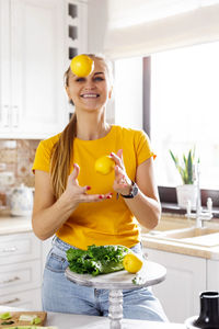 A happy young woman throws a lemon up while cooking healthy food dishes in the kitchen at home.
