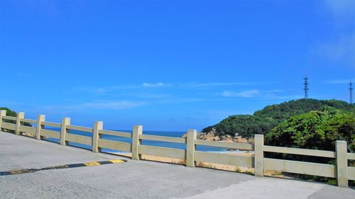 Footpath by railing against blue sky