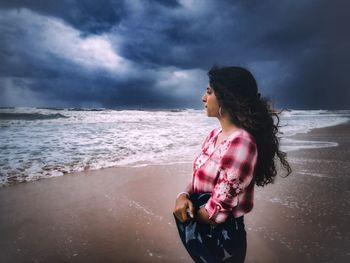 Woman standing at beach against cloudy sky