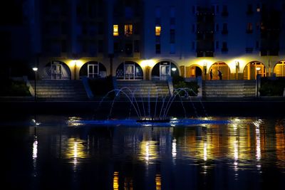 Illuminated building by river at night