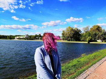 Woman standing by lake against blue sky