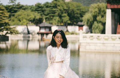 Smiling beautiful woman sitting against lake