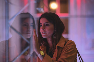 Young woman looking away while standing by glass window