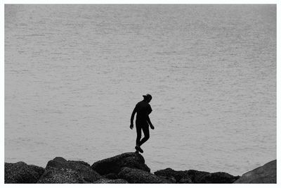 Silhouette man walking on rock formation by sea