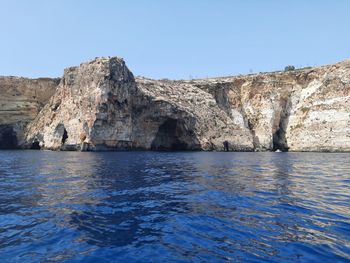 Rock formations by sea against clear blue sky