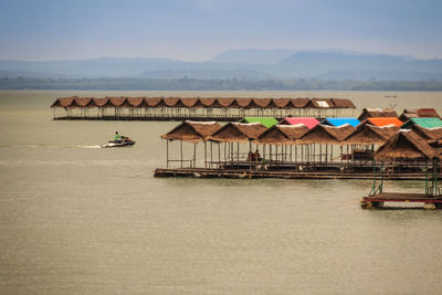 Stilt house on lake by buildings against sky