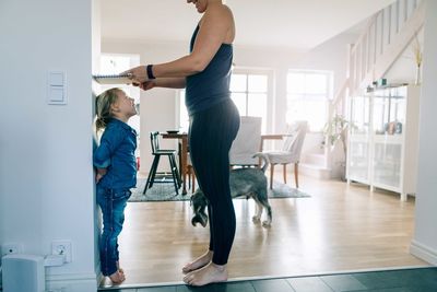 Side view of mother measuring daughter's height with book on wall at home