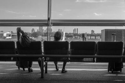 Rear view of people sitting on bench at airport