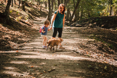 Woman holding hands with daughter while standing by dog in forest