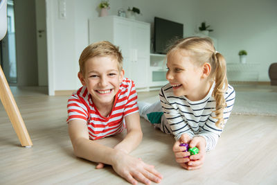 Portrait of cheerful siblings playing with dice while lying on carpet at home