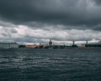 View of city at waterfront against cloudy sky