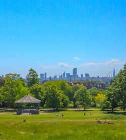 Trees and buildings on field against blue sky