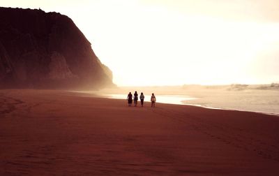 Rear mid distance view of four women walking down sandy beach at sunrise