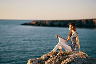 Woman sitting on rock by sea against sky