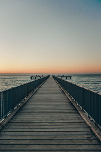 Pier over sea against clear sky during sunset