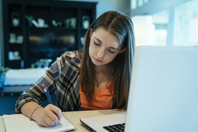 Teenage girl doing homework using laptop computer at home