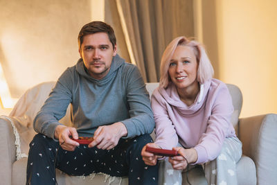 Young family in home clothes playing video games on couch in living room