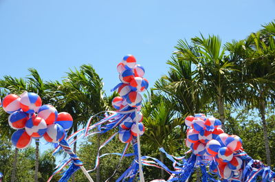 Low angle view of balloons against trees against clear blue sky