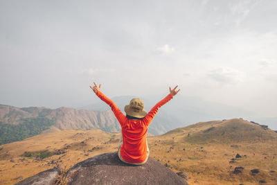 Rear view of person with arms raised against sky