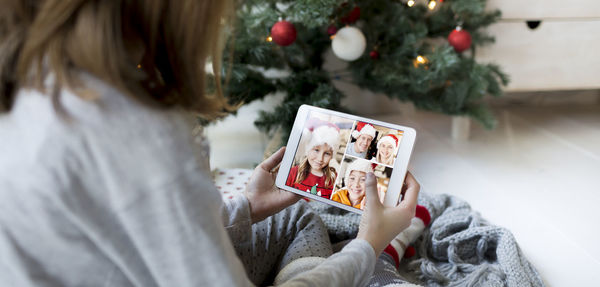 Girl video conferencing while holding digital tablet by christmas tree