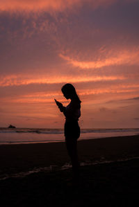 Side view of silhouette teenage girl standing at beach during sunset
