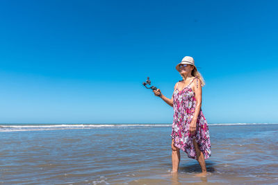 Panoramic photography of a woman walking into the water of the sea while filming with a mobile
