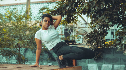 Portrait of woman crouching on edge against trees